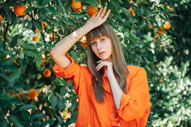 Hermosa chica con vestido naranja posa para la cámara levantando las manos en el jardín naranja