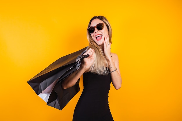 Hermosa chica con vestido negro con bolsas negras sobre fondo amarillo