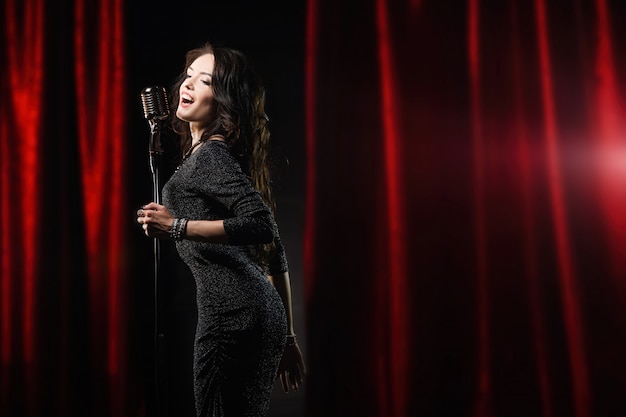 Foto hermosa chica en vestido negro cantando en el micrófono en la sala de conciertos