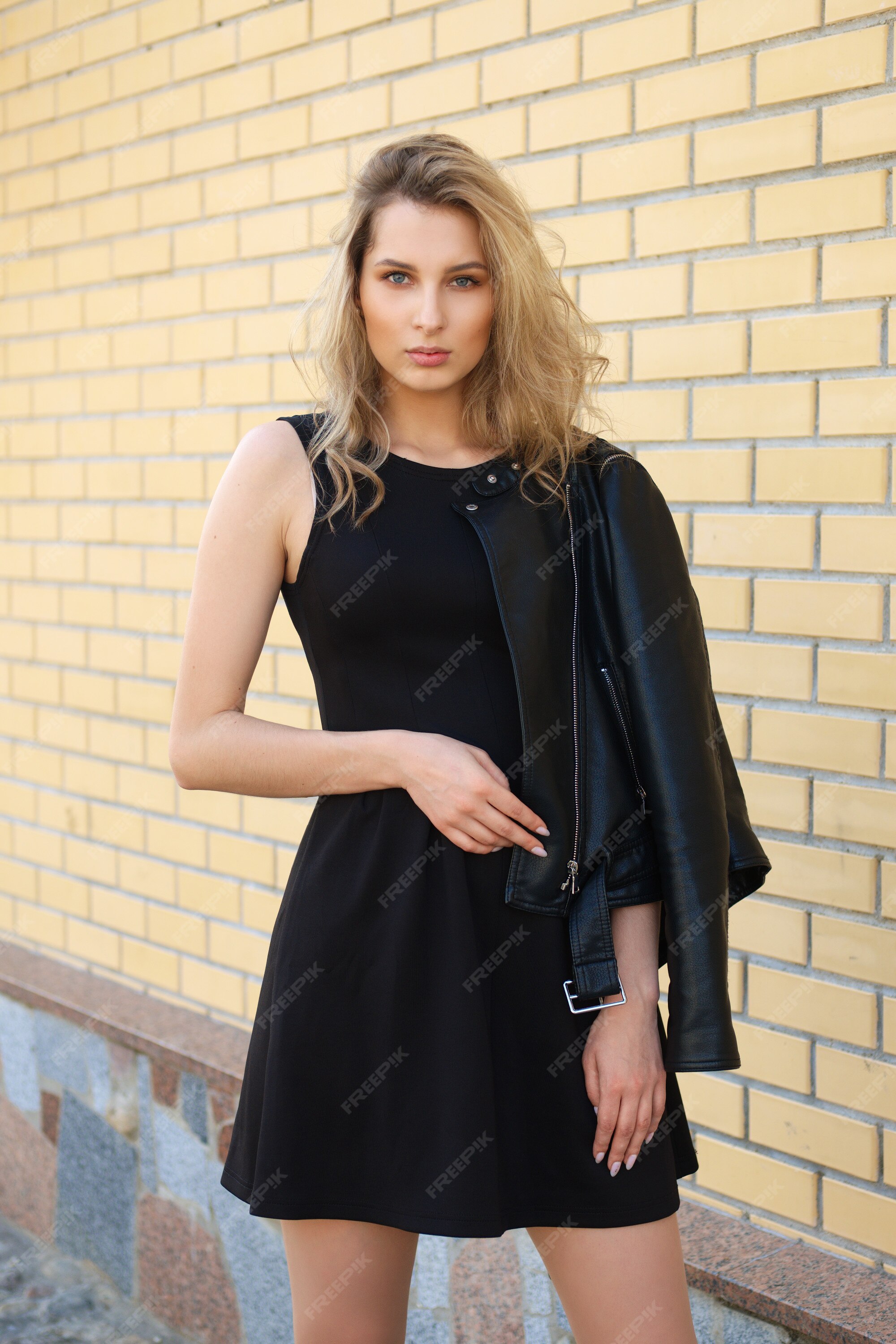 Hermosa chica en vestido negro corto y chaqueta cuero en la calle. | Foto