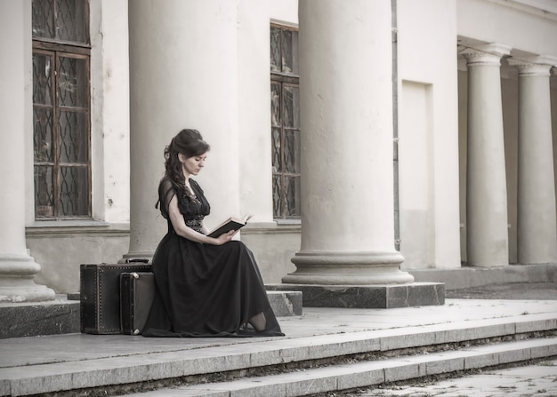 Foto hermosa chica en vestido de noche negro sentado leyendo un libro