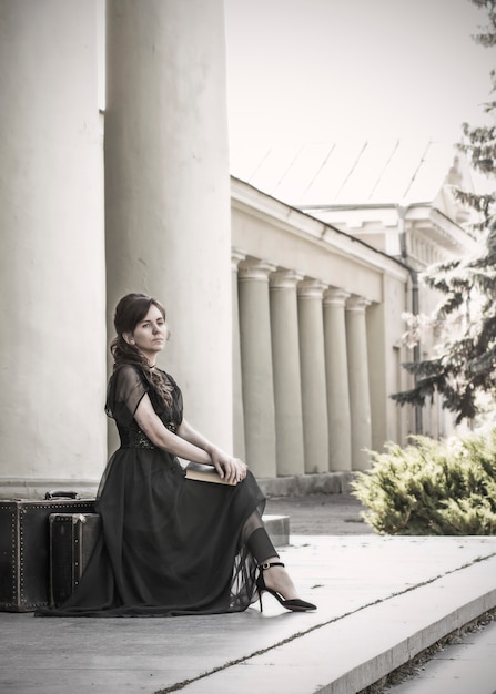 Hermosa chica en un vestido de noche negro se sienta con un libro