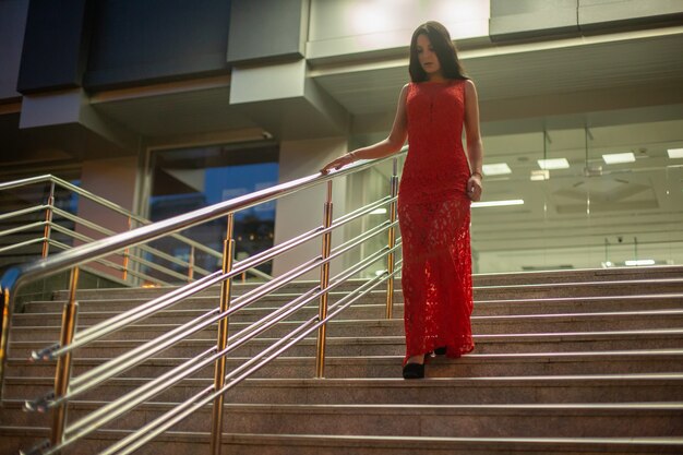 Hermosa chica en vestido de noche rojo baja las escaleras.