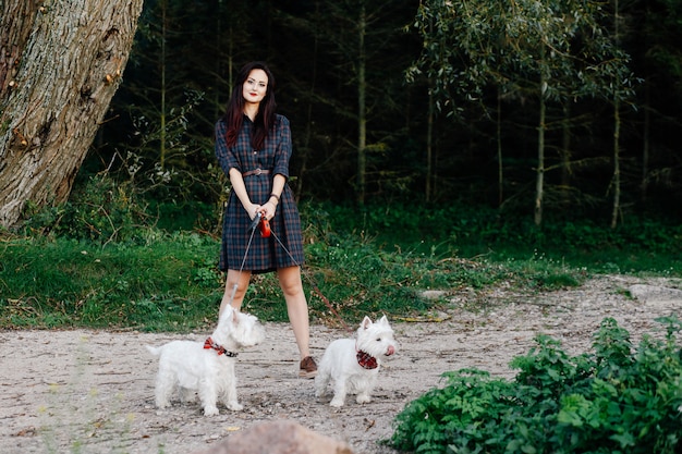 Hermosa chica en un vestido paseando a sus perros blancos en el parque