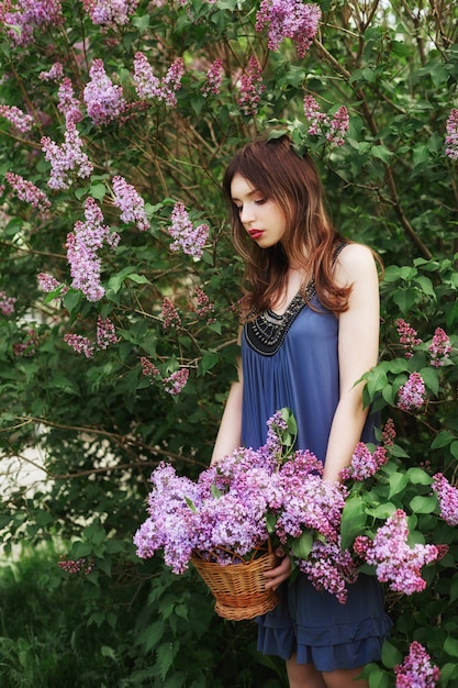 Hermosa chica en un vestido posando en arbusto de lilas.