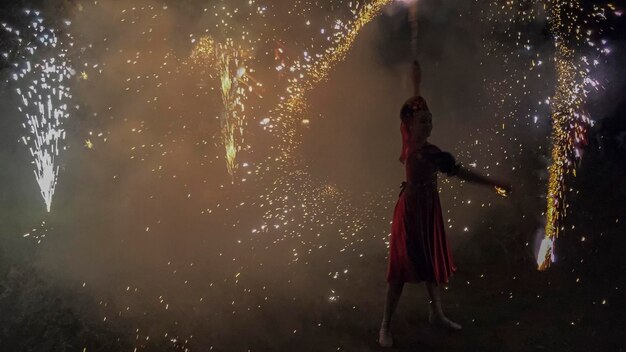 Una hermosa chica con un vestido rojo bailando en medio de fuegos artificiales