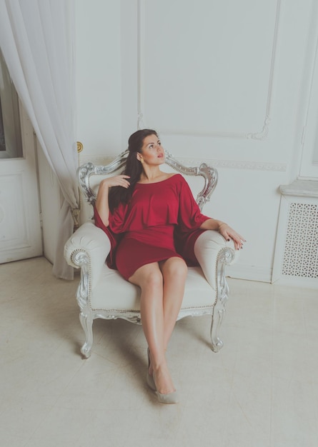 Hermosa chica con vestido rojo posando en una silla vintage.