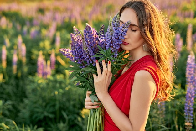 Hermosa chica con un vestido rojo con un ramo de flores de lupino en el campo