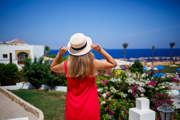 Foto hermosa chica en vestido rojo y sombrero bajo el sol brillante