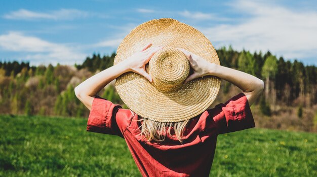 Hermosa chica en vestido rojo y sombrero tiene un tiempo sin preocupaciones en la pradera en las montañas por un bosque. Temporada de primavera