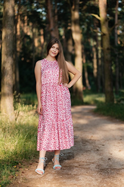 Hermosa chica con vestido rosa de verano en el camino del bosque