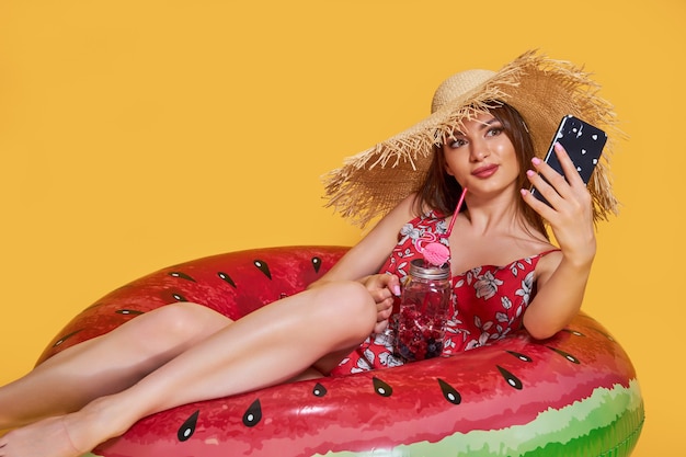 Hermosa chica en vestido de verano sombrero de paja con forma de anillo inflable de sandía con cocktai fresco ...