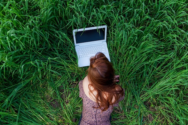 Foto una hermosa chica en un vestido yace y trabaja en una computadora portátil