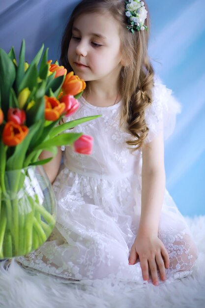 Hermosa chica en vestidos blancos con un magnífico ramo de los primeros tulipanes. Día Internacional de la Mujer. Chica con tulipanes.