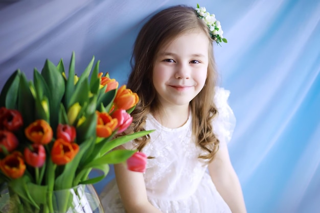 Hermosa chica con vestidos blancos con un magnífico ramo de los primeros tulipanes Día Internacional de la Mujer Chica con tulipanes