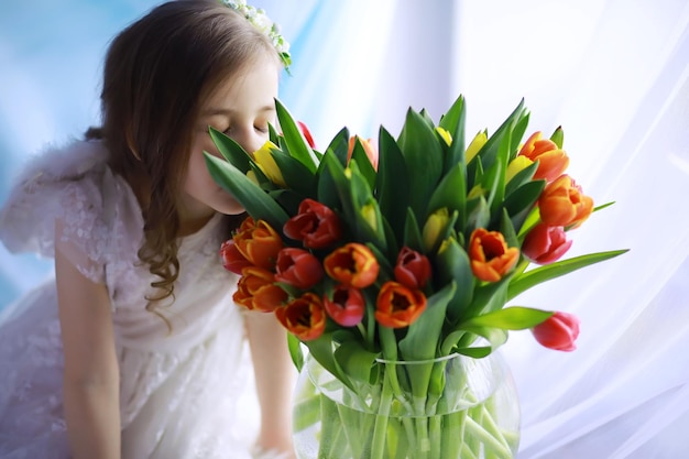 Hermosa chica en vestidos blancos con un magnífico ramo de los primeros tulipanes Día Internacional de la Mujer Chica con tulipanes