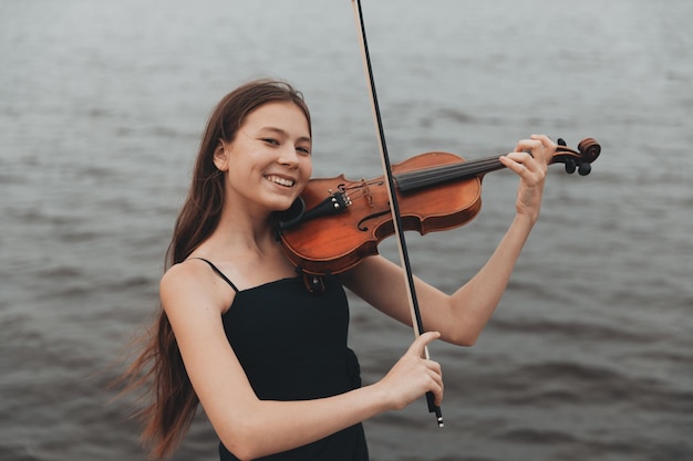 Una hermosa chica con un violín se alza contra el fondo del agua Concepto musical de apariencia asiática Foto de alta calidad