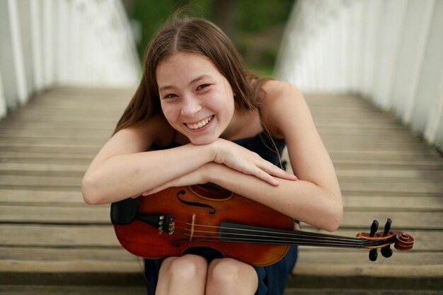 Hermosa chica con violín sonriendo en la naturaleza. Foto de alta calidad