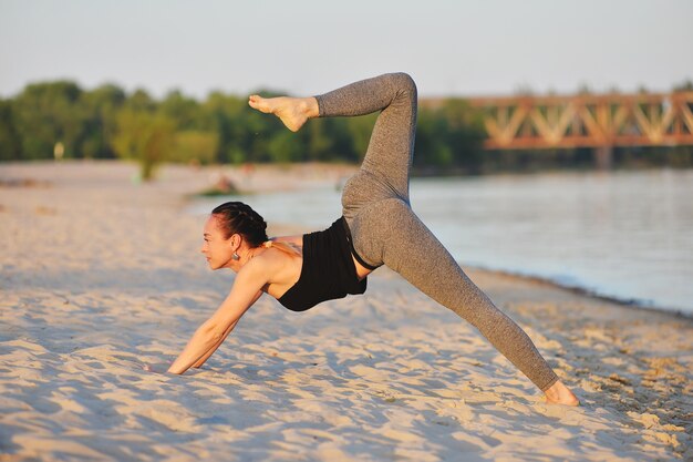 Hermosa chica a yoga en la playa en primavera