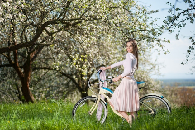 Hermosa ciclista femenina con bicicleta retro en el jardín de primavera