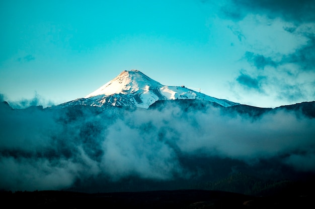 Hermosa cima nevada de las montañas vulcanas con cielo azul y nubes alrededor