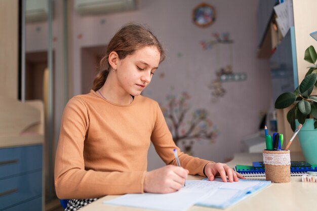 Hermosa colegiala estudiando en casa haciendo los deberes escolares