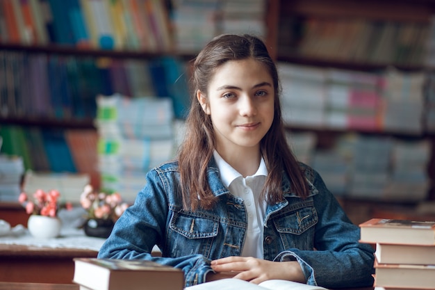 Hermosa colegiala sentada en la biblioteca y leyendo un libro, educación