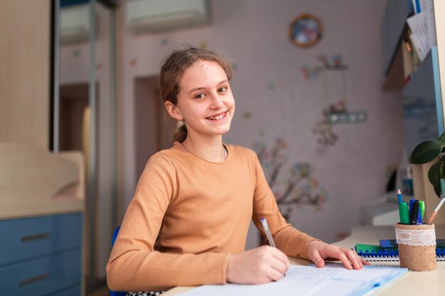 Hermosa colegiala sonriente estudiando en casa haciendo los deberes escolares