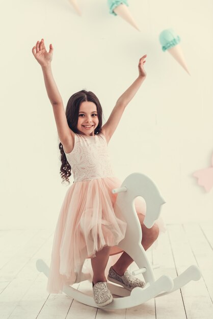 Hermosa colegiala en vestido está sentado en un caballito.