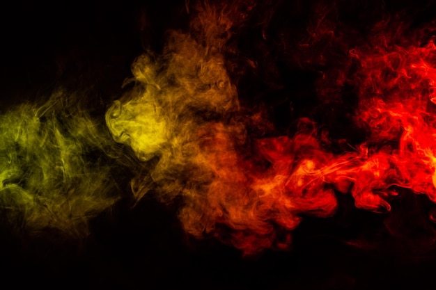 Hermosa columna horizontal de humo en la brillante luz de neón de rojo, verde, amarillo y naranja sobre un fondo negro exhalado del vape Buen patrón para la impresión y el telón de fondo de las ondas de colores