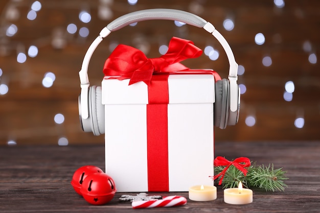 Hermosa composición con caja de regalo y auriculares en la mesa contra luces borrosas. Concepto de música navideña