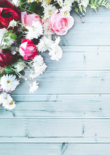 Hermosa composición decorativa vertical de flores sobre una mesa de madera azul. Vista superior, fondo con espacio de copia para su texto. Rosas rojas y rosadas, margaritas blancas.