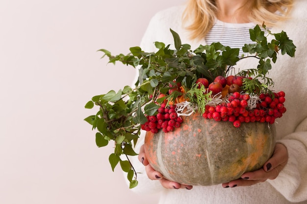 Hermosa composición otoñal en un jarrón de calabaza en manos de mujer Arreglo de flores y frutos rojos