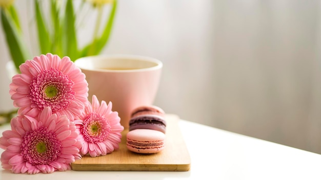 Hermosa composición de pasteles de macarrones con gerberas rosas y una taza rosa con té