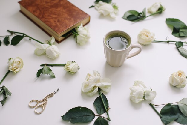Hermosa composición romántica con una taza de té verde matcha y flores rosas sobre fondo blanco.