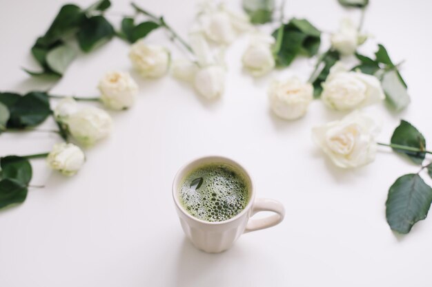 Hermosa composición con taza de té matcha verde y rosas sobre fondo blanco.