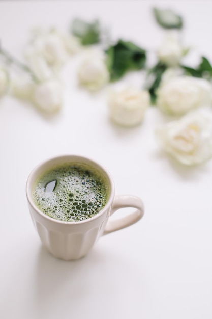 Hermosa composición con taza de té matcha verde y rosas sobre fondo blanco.