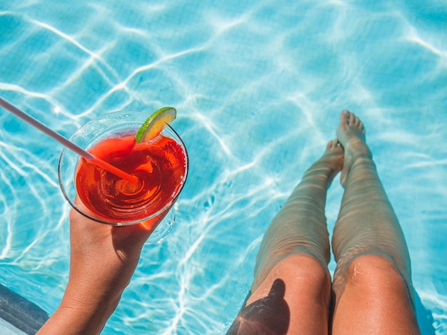 Foto hermosa copa con un cóctel refrescante y una mujer bonita en el fondo de la piscina. vista superior, primer plano. concepto de vacaciones y viajes. momentos de celebración