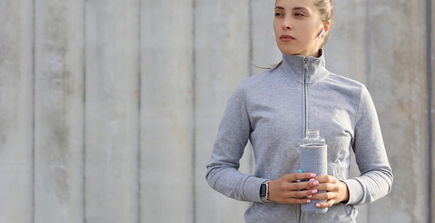 Hermosa corredora está de pie al aire libre sosteniendo una botella de agua. La mujer fitness se toma un descanso después de hacer ejercicio.