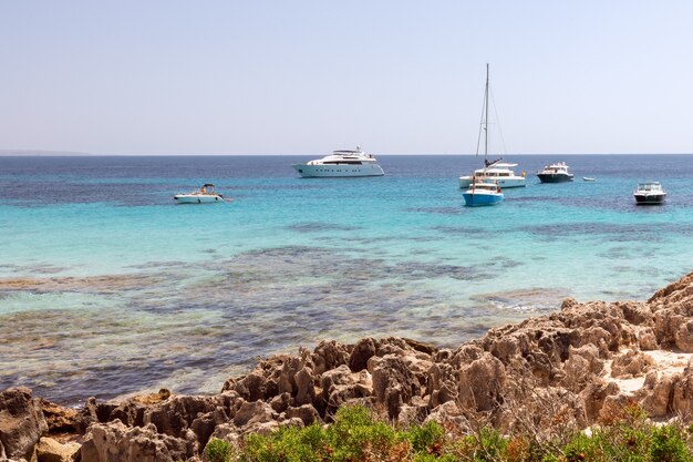 Hermosa costa rocosa y mar turquesa con barcos en Ibiza, España