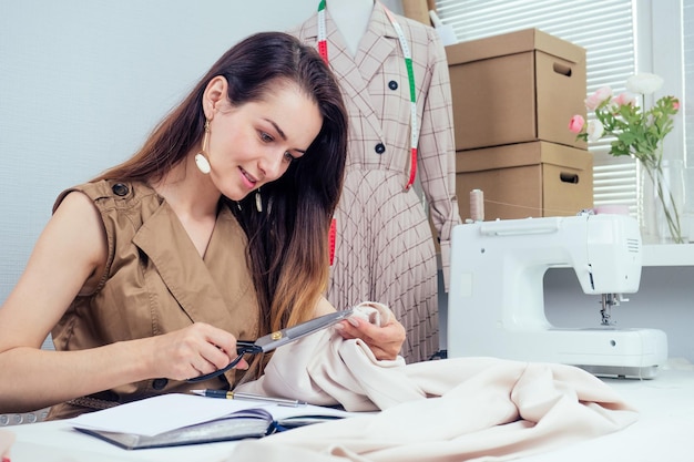 hermosa costurera con cabello largo escribe en un cuaderno. el sastre crea una colección de trajes. ropa de diseñador de mujer joven notas ideas en cuaderno