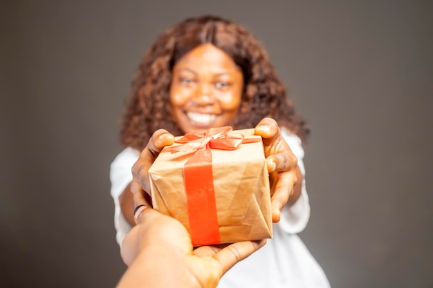 Hermosa dama africana recibiendo una caja de regalo envuelta de pie sobre un fondo de estudio