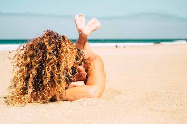 Hermosa dama bronceada atractiva de mediana edad con cabello rubio rizado se acuesta en la playa para un baño de sol de verano durante las vacaciones