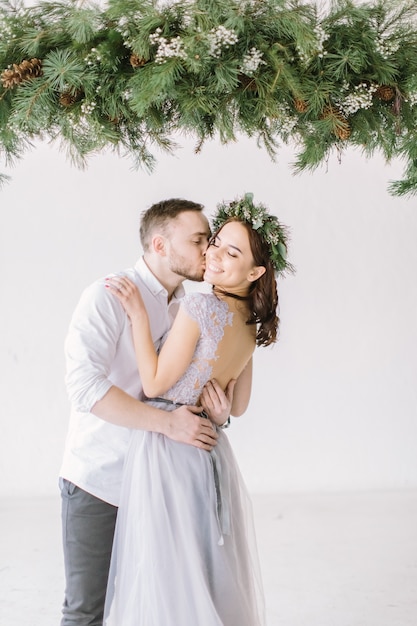 Hermosa dama de honor en corona de pino y vestido gris con apuesto padrino de boda en el estudio abrazando