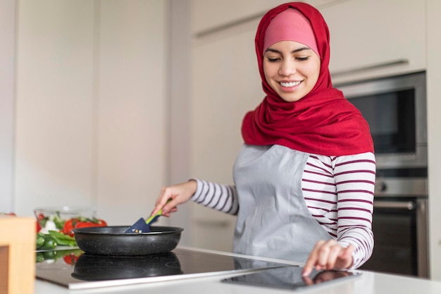 Hermosa dama musulmana cocinando en casa leyendo un blog culinario