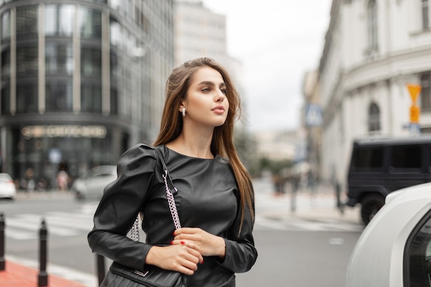 Hermosa dama de negocios elegante con ropa negra de moda con un vestido y una bolsa camina en una ciudad moderna Mujer muy elegante