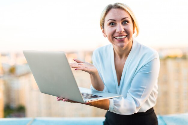 Hermosa dama de negocios inteligente de pie en el techo con la computadora portátil en las manos