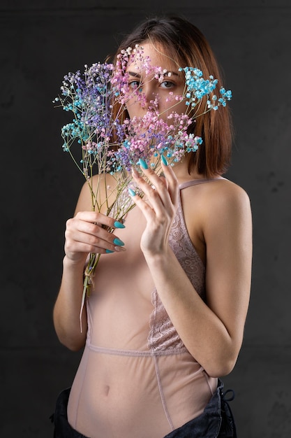 Una hermosa dama sexy en un elegante traje desnudo sostiene flores en sus manos Retrato de belleza de moda de una chica modelo de moda en el estudio