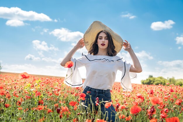 Hermosa dama ucraniana sola en sombrero de paja en el campo de amapolas de flores, sexy, día soleado