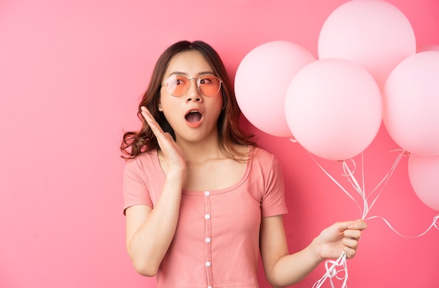 La hermosa dama usa lentes y sostiene globos en un rosa.